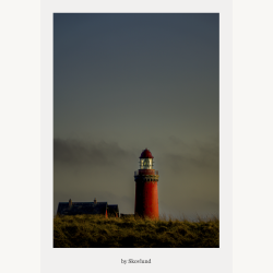 R�dt fyrt�rn st�ende i klitterne under himmel i den bl� time, med lys i lanternen og d�mpet aftensstemning.