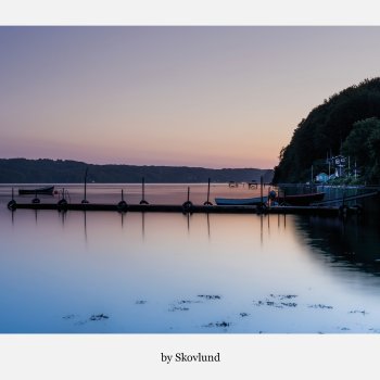 Stille solnedgang ved Ulb�khus med spejlblankt vand, b�de ved bro og bl�de farver over Vejle Fjord i aftenslys.