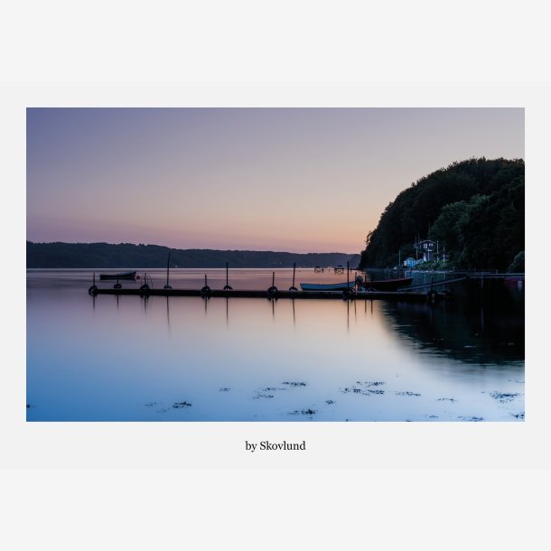 Stille solnedgang ved Ulb�khus med spejlblankt vand, b�de ved bro og bl�de farver over Vejle Fjord i aftenslys.