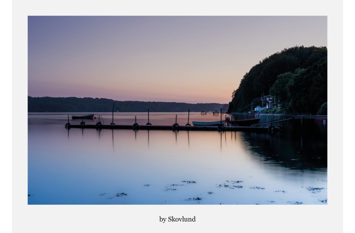 Stille solnedgang ved Ulb�khus med spejlblankt vand, b�de ved bro og bl�de farver over Vejle Fjord i aftenslys.