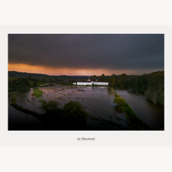 Haraldsk�r beliggende i en oversv�mmet eng under en br�ndende himmel med regntunge skyer, hvor vand, lys og landskab smelter sammen i et dramatisk, nordisk udtryk.
